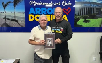 Arroio do Silva: livreto celebra centenária Dona Eulina O prefeito de Balneário Arroio do Silva, Jorge Luiz Freitas, à direita, recebe do neto de Dona Eulina, Everson (Xande), o livreto de versos em homenagem aos 101 anos da moradora centenária. Ambos seguram a obra literária em frente a um painel institucional do município.