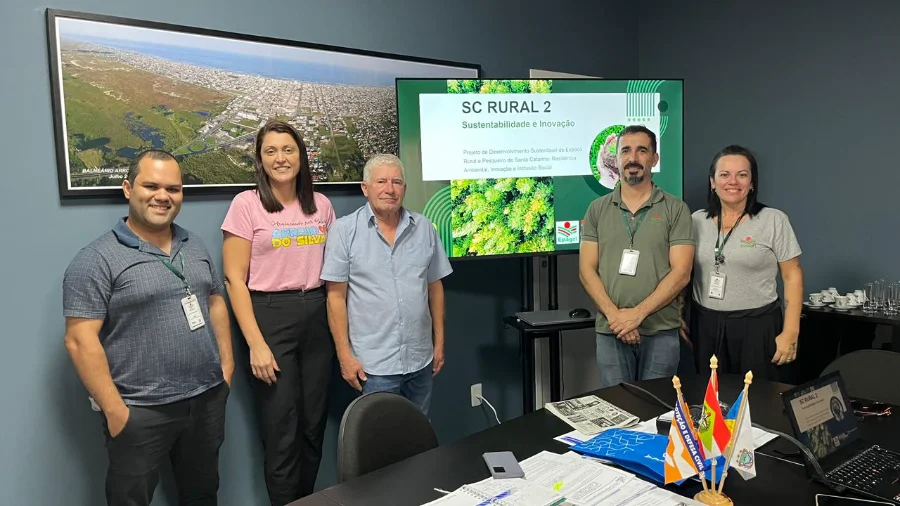 Representantes da Epagri, o prefeito Jorge Luiz Freitas e a secretária Itaionara Recco durante reunião na Prefeitura de Balneário Arroio do Silva. Ao fundo, uma tela exibe o projeto SC Rural 2 com os dizeres Sustentabilidade e Inovação, destacando o planejamento para o setor rural e pesqueiro do município.