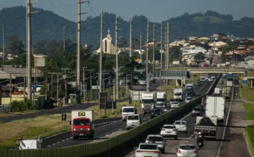 BR-101 Sul deve receber 635 mil veículos no feriado Vista aérea do tráfego intenso de carros e caminhões na rodovia BR-101 Sul em Santa Catarina, mostrando o fluxo de veículos em trecho duplicado próximo a áreas urbanas sob concessão da ViaCosteira.