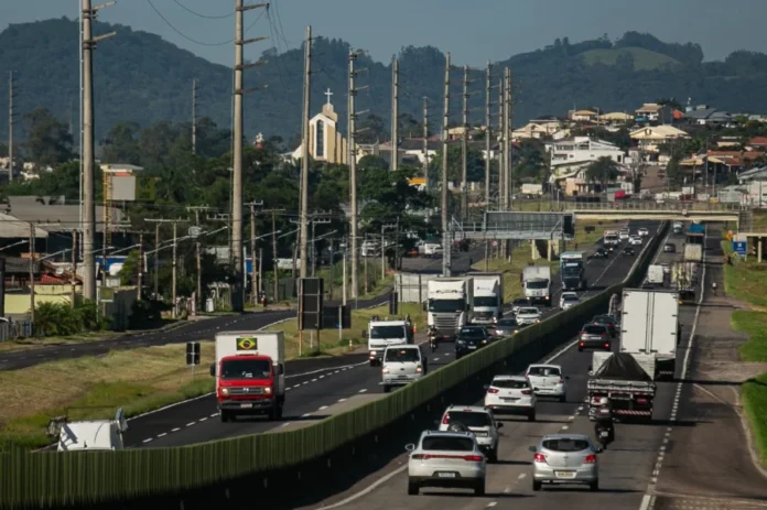 BR-101 Sul deve receber 635 mil veículos no feriado Vista aérea do tráfego intenso de carros e caminhões na rodovia BR-101 Sul em Santa Catarina, mostrando o fluxo de veículos em trecho duplicado próximo a áreas urbanas sob concessão da ViaCosteira.