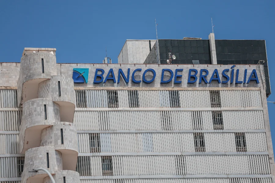 Fachada externa do edifício da sede do Banco de Brasília (BRB) em Brasília, com destaque para o letreiro azul da instituição e arquitetura moderna sob céu limpo. Imagem focada em economia, mercado financeiro e gestão pública do Distrito Federal.
