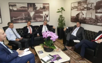 Bancada do Sul debate Rio Urussanga e custo do gás na Alesc Deputados estaduais da Bancada do Sul reunidos em gabinete na Alesc para debater o desassoreamento do Rio Urussanga e o custo do gás natural. Na cena, parlamentares conversam sentados em sofás pretos ao redor de uma mesa com orquídeas e documentos.