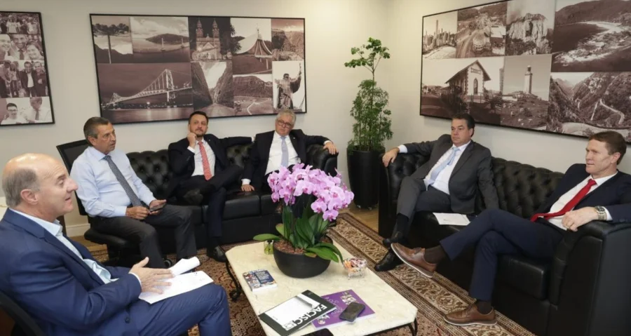 Bancada do Sul debate Rio Urussanga e custo do gás na Alesc Deputados estaduais da Bancada do Sul reunidos em gabinete na Alesc para debater o desassoreamento do Rio Urussanga e o custo do gás natural. Na cena, parlamentares conversam sentados em sofás pretos ao redor de uma mesa com orquídeas e documentos.