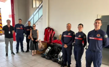 Bombeiros de Forquilhinha recebem R$ 65 mil em equipamentos Entrega simbólica de novos equipamentos operacionais e de prevenção para o Corpo de Bombeiros de Forquilhinha (CBMSC) em parceria com o MPSC. A promotora de Justiça Rafaela Póvoas Cardozo Lehmann e oficiais posam com os materiais doados, incluindo manequins de RCP, Equipamentos de Proteção Respiratória (EPRs), capacetes e roupas de neoprene, no interior de um quartel.