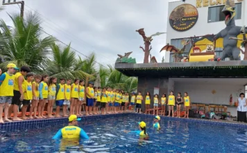 Bombeiros de SC formam 7,6 mil crianças contra afogamento Crianças com uniformes amarelos do Projeto Golfinho enfileiradas na borda de uma piscina recebendo instruções de segurança aquática de instrutores do CBMSC dentro da água para prevenção de afogamentos em Santa Catarina.