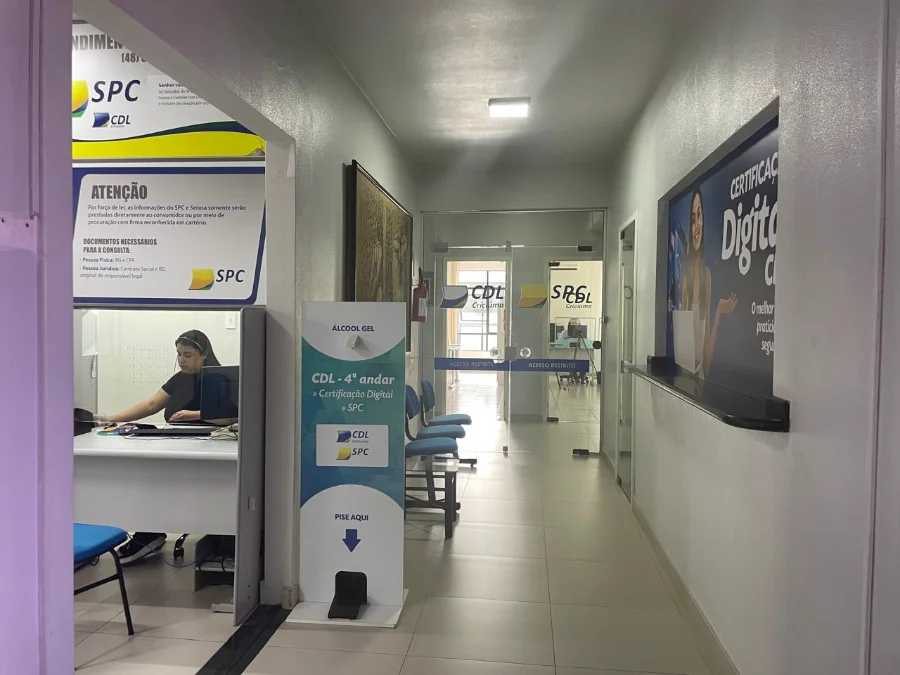 Interior da recepção da CDL Criciúma com balcões de atendimento, sinalização do SPC e totens informativos, representando a estrutura de apoio ao mercado de trabalho e ao programa CDL Talentos.