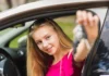 Jovem loira sorrindo no banco do motorista de um carro, estendendo as chaves pela janela. Cena ilustrativa sobre o debate de redução da idade mínima para CNH.