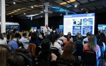 CNM reúne mil gestores em Criciúma para qualificar gestão Público de gestores e servidores municipais utilizando fones de ouvido durante palestra na imersão Conexão CNM em Criciúma. Ao fundo, palestrante apresenta painel sobre ferramentas de gestão pública municipal e recursos da Confederação Nacional de Municípios.