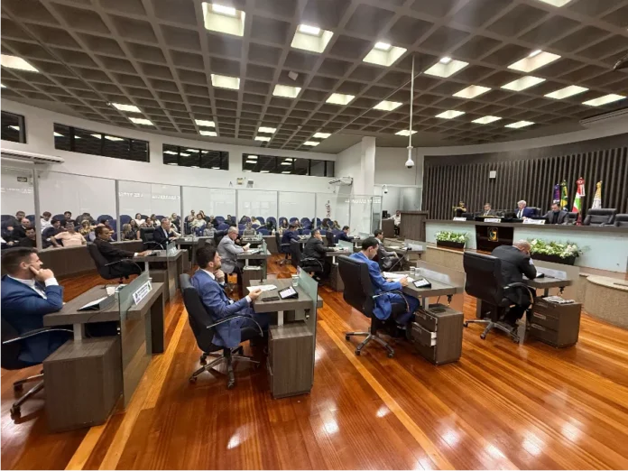 Câmara de Araranguá aprova reajuste de 4,2% para servidores Sessão ordinária na Câmara de Vereadores de Araranguá para votação do reajuste salarial de 4,2% dos servidores municipais. A imagem mostra parlamentares sentados em suas bancadas no plenário e público acompanhando a sessão ao fundo.