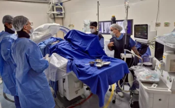 Cirurgias eletivas crescem 46% no Instituto de Cardiologia Profissionais de saúde realizam procedimento de hemodinâmica no Instituto de Cardiologia de Santa Catarina (ICSC). A imagem detalha a equipe médica com trajes cirúrgicos operando equipamentos de alta tecnologia e monitores em uma sala de cirurgia cardiovascular moderna.