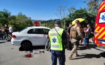 Colisão entre carro e moto deixa ferido em Morro da Fumaça Acidente de trânsito em Morro da Fumaça envolvendo colisão lateral entre carro branco e motocicleta no bairro Estação Cocal. A imagem mostra bombeiro militar e policial militar atendendo a ocorrência próximo a uma ambulância.