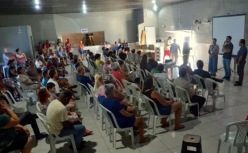 Colônia Z33 recebe equipamentos e debate crédito no Rincão Mais de 200 pescadores artesanais assistem a uma reunião da Colônia Z33 em Balneário Rincão, SC, onde estão sendo apresentados novos equipamentos multimídia. No palco, oradores falam diante de uma tela de projeção. O público está sentado em cadeiras de plástico. Ao fundo, um balcão com letreiro BAR.