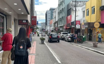 Comércio de Criciúma espera alta nas vendas de Dia das Mães Rua movimentada no centro comercial de Criciúma com fachadas de lojas, pedestres caminhando e carros estacionados, ilustrando o movimento do varejo para as compras de Dia das Mães.