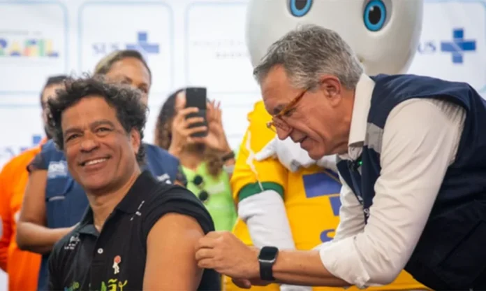 Copa 2026 Saúde lança campanha de vacina contra sarampo Ministro da Saúde Alexandre Padilha aplica vacina contra o sarampo no ex-jogador Raí durante lançamento da campanha "Vacinar é muito Brasil" para a Copa do Mundo 2026, com o personagem Zé Gotinha ao fundo.