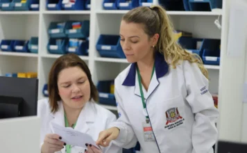 Criciúma é selecionada para projeto nacional do SUS Duas profissionais da Secretaria Municipal de Saúde de Criciúma, vestindo jalecos brancos, analisam um documento técnico em uma farmácia municipal. Ao fundo, prateleiras organizadas com insumos médicos representam a estrutura de atendimento do SUS em Criciúma, destacando a qualificação e a educação permanente em saúde.