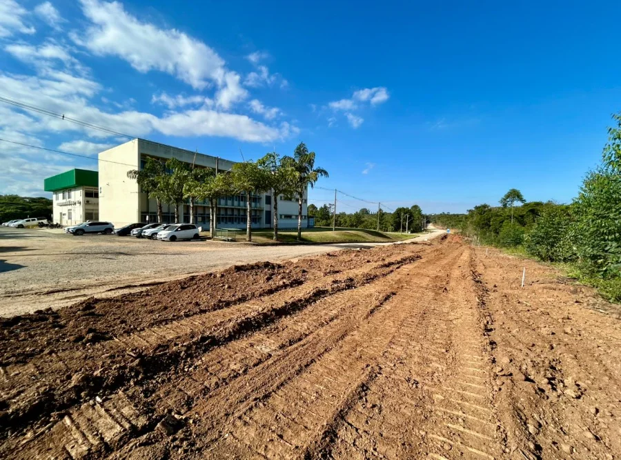 Vista aérea das obras de terraplanagem da nova via de ligação entre as rodovias Governador Jorge Lacerda e Antônio Just em Criciúma, mostrando o traçado de terra ao lado do Centro Tecnológico Satc sob céu azul.