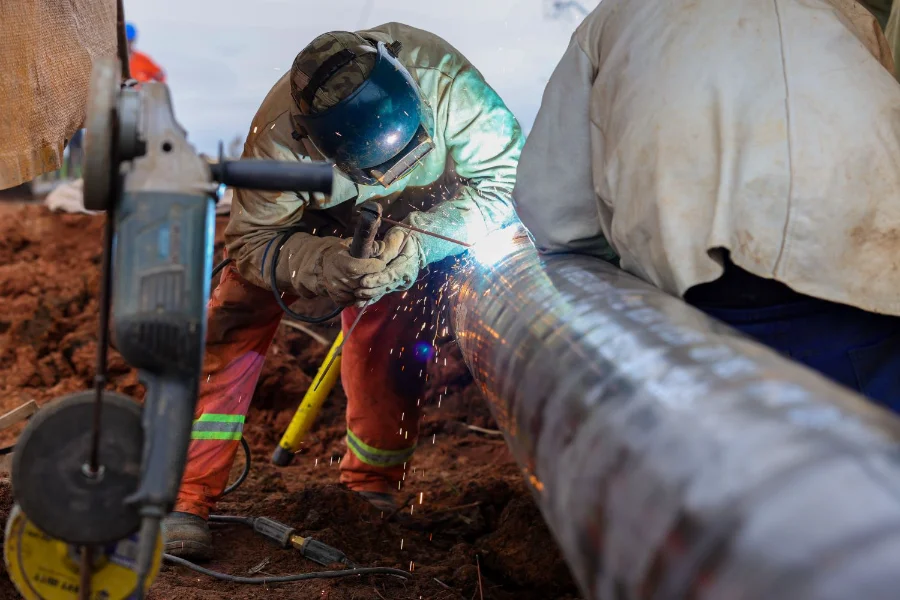 Trabalhador especializado realiza soldagem em tubulação de aço da rede de gás natural da SCGÁS em Santa Catarina. A imagem destaca a expansão da infraestrutura de distribuição de energia para atender polos industriais catarinenses.