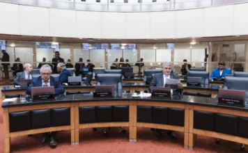 Deputados cobram rigor em sabatina de indicado ao STF Uma fotografia de uma sessão plenária na Assembleia Legislativa de Santa Catarina (Alesc). Deputados estaduais de Santa Catarina, incluindo o Deputado Mauro de Nadal (em terno azul ao fundo) e o Deputado Tiago Zeilli (segundo da esquerda), estão sentados em bancadas semicirculares e acolchoadas. Um deputado no centro lê um jornal ("Diarino"), enquanto outros trabalham em notebooks. O plenário é moderno com divisórias de vidro no fundo onde se vê mais pessoas. A imagem captura o ambiente de debates parlamentares sobre segurança pública e política estadual.