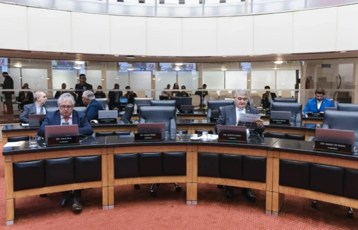 Deputados cobram rigor em sabatina de indicado ao STF Uma fotografia de uma sessão plenária na Assembleia Legislativa de Santa Catarina (Alesc). Deputados estaduais de Santa Catarina, incluindo o Deputado Mauro de Nadal (em terno azul ao fundo) e o Deputado Tiago Zeilli (segundo da esquerda), estão sentados em bancadas semicirculares e acolchoadas. Um deputado no centro lê um jornal ("Diarino"), enquanto outros trabalham em notebooks. O plenário é moderno com divisórias de vidro no fundo onde se vê mais pessoas. A imagem captura o ambiente de debates parlamentares sobre segurança pública e política estadual.