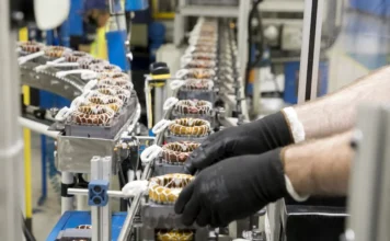 Economia de SC fica estável no primeiro bimestre de 2026 Linha de produção industrial em Santa Catarina com trabalhadores manuseando componentes de motores elétricos em fábrica catarinense. A imagem ilustra o setor da indústria de SC, que apresentou retração no início de 2026 devido às taxas de juros.