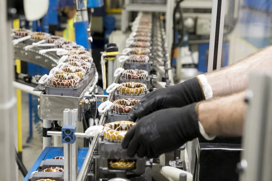 Linha de produção industrial em Santa Catarina com trabalhadores manuseando componentes de motores elétricos em fábrica catarinense. A imagem ilustra o setor da indústria de SC, que apresentou retração no início de 2026 devido às taxas de juros.