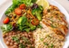 Prato de alimentação saudável e equilibrada contendo peito de frango grelhado fatiado, arroz integral, feijão e salada colorida com brócolis, alface e tomates cereja. Foto foca no conceito de déficit calórico com densidade nutricional.