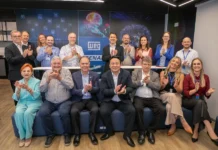 FIESC e WEG ampliam cooperação em ensino profissional Lideranças da FIESC, WEG e SENAI posam juntas e batem palmas em um centro de formação em Jaraguá do Sul, Santa Catarina, celebrando parceria e investimentos. Os logos da WEG e SENAI são visíveis no painel de fundo tecnológico.