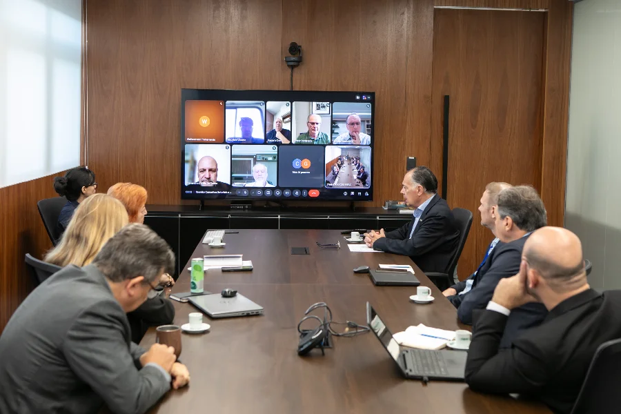 FIESC reformula fóruns e cria novos conselhos industriais Reunião da diretoria da FIESC em Florianópolis para discussão da nova estrutura de conselhos industriais, com executivos ao redor de uma mesa de conferência e participantes via videochamada em uma tela ao fundo.