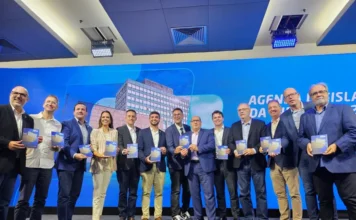 Fiergs entrega Agenda Legislativa 2026 à Assembleia Deputado Sergio Peres, Claudio Bier e parlamentares gaúchos posam segurando exemplares da Agenda Legislativa 2026 da Fiergs durante entrega oficial em Porto Alegre. O grupo está em um palco à frente de um telão azul que exibe a sede da federação.