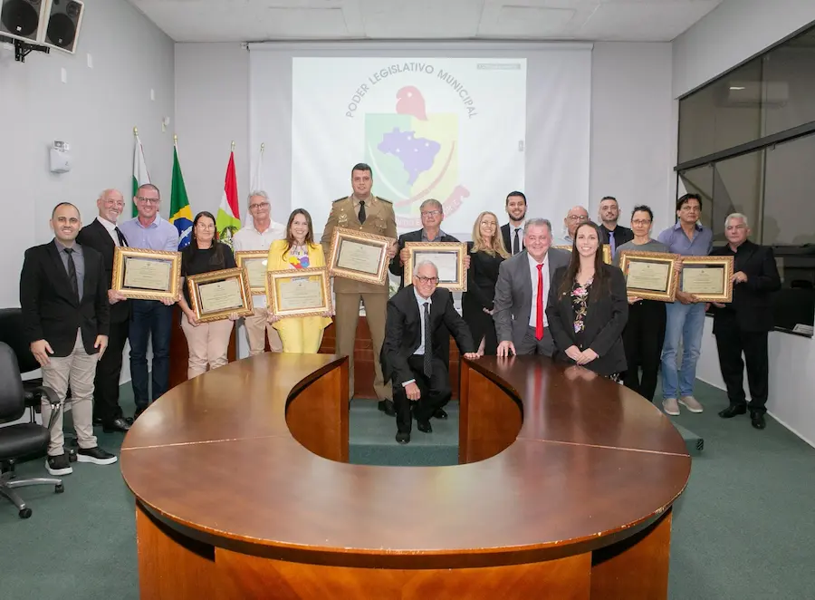 Homenageados e autoridades locais seguram certificados durante sessão solene na Câmara de Vereadores em celebração aos 37 anos de emancipação de Forquilhinha, Santa Catarina.