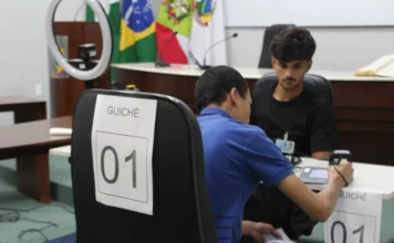 Forquilhinha registra 257 atendimentos em ação eleitoral Atendimento eleitoral sendo realizado em guichê na Câmara de Vereadores de Forquilhinha, com cidadão utilizando dispositivo eletrônico de biometria e assinatura para regularização de título de eleitor.