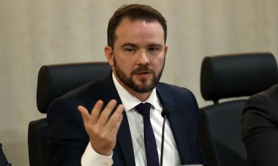 Governo prepara novo Desenrola com uso de FGTS para dívidas O ministro da Fazenda em exercício, Dario Durigan, gesticula com a mão direita enquanto fala em uma mesa de conferência sobre o novo programa Desenrola e o uso do FGTS para renegociação de dívidas.