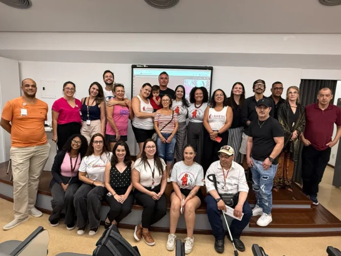 Hemosc realiza encontro sobre desafios da hemofilia em SC Ampla foto de grupo de pacientes com hemofilia, familiares e profissionais de saúde reunidos no auditório do Hemosc em Florianópolis para o IV Encontro da Hemofilia. A cena mostra a comunidade unida na frente de uma tela de projeção, celebrando o Dia Mundial da Hemofilia e a parceria com a Ahesc.