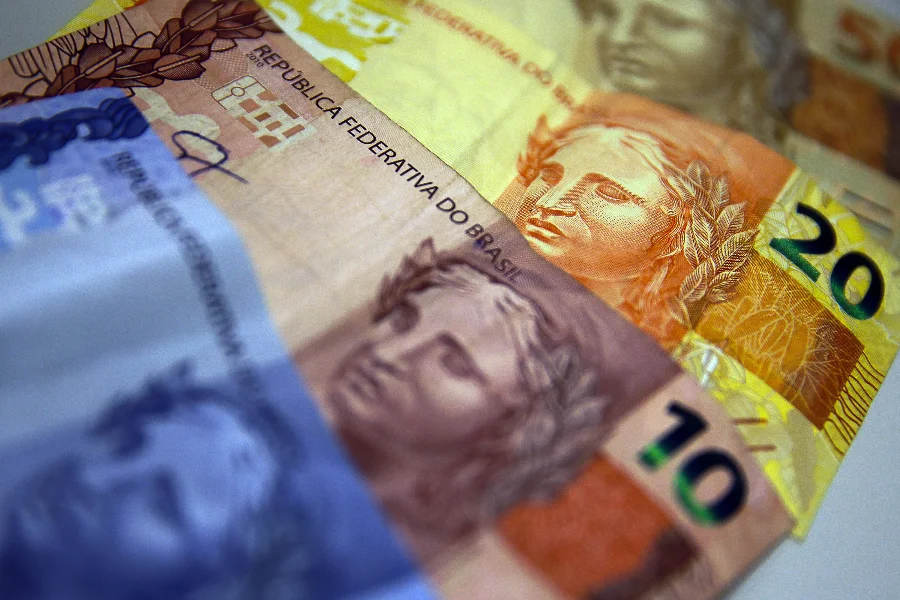 Cédulas de Real brasileiras em destaque, com notas de 10, 20 e 50 reais sobrepostas, representando o planejamento financeiro e a restituição do Imposto de Renda 2026 da Receita Federal.