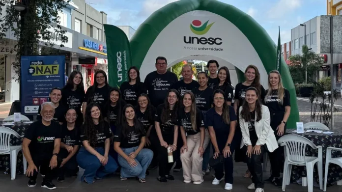 IR na Praça orienta contribuintes e bate recorde de doações Grupo de estudantes e professores de Ciências Contábeis da Unesc e integrantes do NAF reunidos em frente a um portal inflável da universidade durante o evento Imposto de Renda na Praça em Araranguá, vestindo camisetas pretas com a frase Contador com Orgulho.