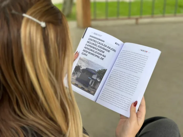 Içara é destaque em livro da FECAM sobre educação inclusiva Pessoa com cabelos loiros vista de costas lendo o livro Práticas que Inspiram da FECAM, aberto na página que destaca o Centro Cacilda Dajori e o projeto de educação inclusiva e aprendizagem personalizada da rede municipal de Içara.