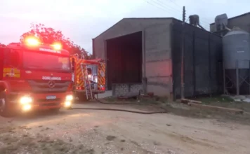 Incêndio atinge silo de grãos em Içara nesta quarta-feira Caminhão de bombeiros (ABTR-208 do CBMSC) com luzes de emergência acesas em frente a um silo de grãos e uma edificação industrial de concreto em Içara, SC. Mangueiras de incêndio no chão indicam o combate a incêndio no local no bairro Vila Nova.