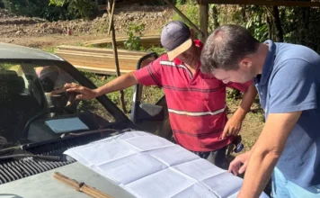 Jacinto Machado inicia construção de 11 novas pontes Engenheiro Bruno Nagel e técnico analisam planta do projeto de construção das cabeceiras para kits ponte sobre o capô de um carro em canteiro de obras em Jacinto Machado.