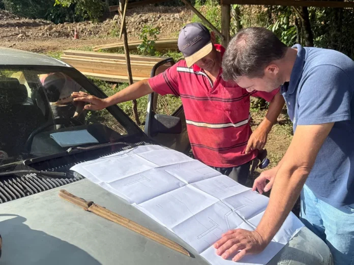 Jacinto Machado inicia construção de 11 novas pontes Engenheiro Bruno Nagel e técnico analisam planta do projeto de construção das cabeceiras para kits ponte sobre o capô de um carro em canteiro de obras em Jacinto Machado.