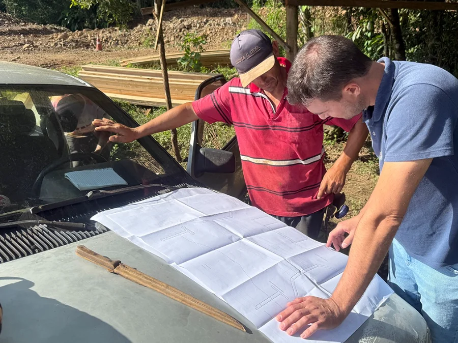 Jacinto Machado inicia construção de 11 novas pontes Engenheiro Bruno Nagel e técnico analisam planta do projeto de construção das cabeceiras para kits ponte sobre o capô de um carro em canteiro de obras em Jacinto Machado.