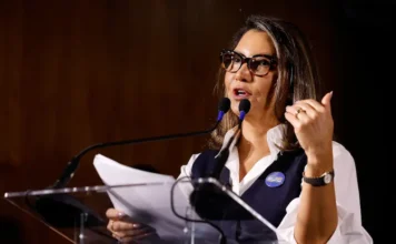 Janja vincula falta de regulação de redes à morte de mulheres A primeira-dama Janja da Silva discursa em evento institucional usando botom da campanha "Brasil contra o Feminicídio". A imagem ilustra seu engajamento em políticas de proteção à mulher, tema central de seu recente discurso em Barcelona.
