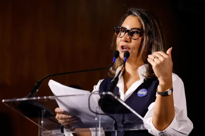 Janja vincula falta de regulação de redes à morte de mulheres A primeira-dama Janja da Silva discursa em evento institucional usando botom da campanha "Brasil contra o Feminicídio". A imagem ilustra seu engajamento em políticas de proteção à mulher, tema central de seu recente discurso em Barcelona.