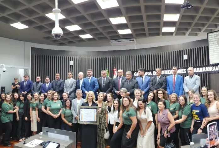 Luciane Ceretta recebe título de cidadã araranguaense Profª. Drª. Luciane Ceretta segura o quadro de Cidadã Honorária cercada por vereadores e equipe técnica na Câmara de Vereadores de Araranguá durante sessão solene.