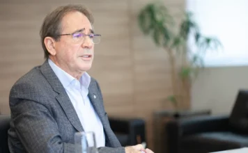 Mario Cezar de Aguiar recebe maior comenda da CNI em SC Mario Cezar de Aguiar, ex-presidente da FIESC e vice-presidente da CNI, veste terno cinza e camisaria clara, gesticulando enquanto fala em ambiente profissional. O industrial será homenageado com a Ordem do Mérito Industrial da CNI em Santa Catarina.