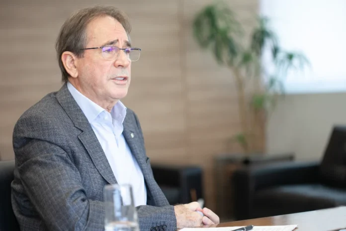 Mario Cezar de Aguiar recebe maior comenda da CNI em SC Mario Cezar de Aguiar, ex-presidente da FIESC e vice-presidente da CNI, veste terno cinza e camisaria clara, gesticulando enquanto fala em ambiente profissional. O industrial será homenageado com a Ordem do Mérito Industrial da CNI em Santa Catarina.