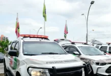 Motorista embriagado é preso após causar acidente em Criciúma Viaturas da Polícia Militar de Santa Catarina (PMSC) caracterizadas e estacionadas com o giroflex aceso, em frente a mastros com bandeiras, ilustrando operações policiais e a presença da força de segurança no estado.