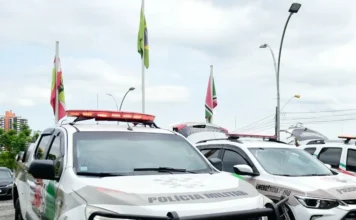 Motorista embriagado é preso após causar acidente em Criciúma Viaturas da Polícia Militar de Santa Catarina (PMSC) caracterizadas e estacionadas com o giroflex aceso, em frente a mastros com bandeiras, ilustrando operações policiais e a presença da força de segurança no estado.