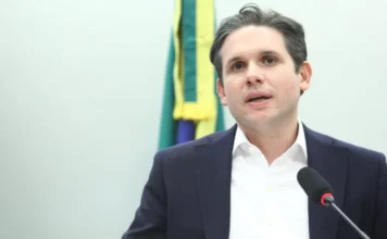 Motta cria comissão para analisar fim da escala 6×1 O deputado federal Hugo Motta, presidente da Câmara dos Deputados, fala ao microfone durante pronunciamento sobre a criação da comissão especial para analisar o fim da escala 6x1. Ao fundo, detalhes da bandeira do Brasil.