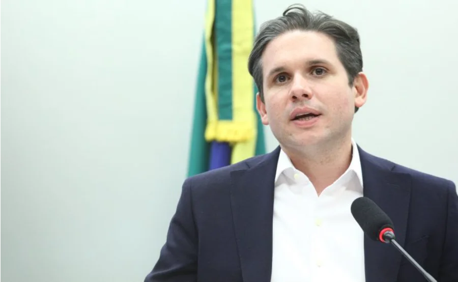 O deputado federal Hugo Motta, presidente da Câmara dos Deputados, fala ao microfone durante pronunciamento sobre a criação da comissão especial para analisar o fim da escala 6x1. Ao fundo, detalhes da bandeira do Brasil.