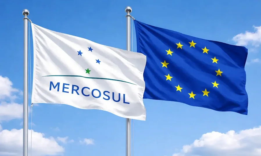 Bandeiras do Mercosul e da União Europeia hasteadas lado a lado sob céu azul, representando a relação comercial e as exigências do regulamento EUDR para a exportação de commodities brasileiras.